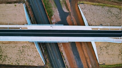 top down drone shot of a road bridge crossing over the train tracks