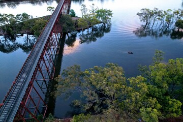 drone shot of a boat at sunset on a river with a train bridge