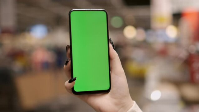 young woman hand using smart phone with green screen in the market. close-up chroma key mock up hypermarket. woman holding phone with green screen in the mall. shopping in the mall