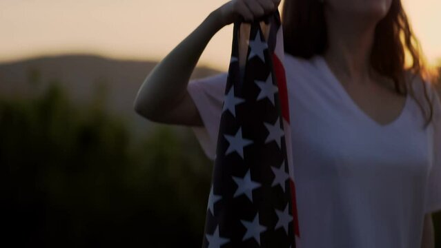 A young happy woman raises her hand with the American flag. In the background of the sunset sky. Slow motion. Jib shot. Blurred. Independence Day Concept.