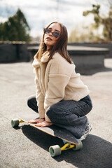 Young brunette squatting near skateboard on rooftop