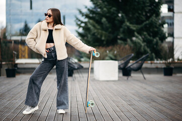 Fototapeta na wymiar Woman in street clothes posing with skateboard in hands