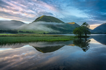A misty tranquil and peaceful morning by a lake with reflections and mist drifting by, in the Lake District