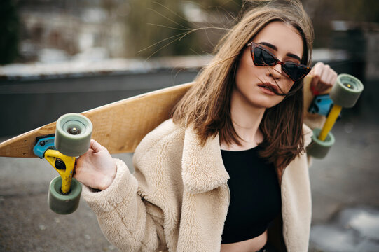 Young brunette in sunglasses posing on roof with skateboard