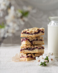 Stacked homemade fruit jam cookies served with bottle of milk on textile background, selective focus