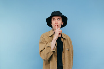 Funny guy in panama and shirt stands on a blue background, looks away and shows a gesture of...