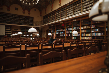 Woman sits alone in a beautiful old public library at a table and reads a book.