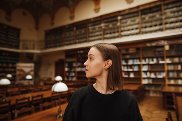 Portrait of a beautiful woman with a serious face standing in a public library and looking away with a serious face