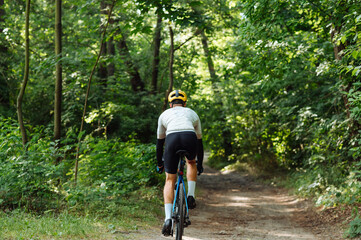 Obraz premium Male cyclist rides on the road of the forest on a bicycle, view from the back.