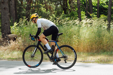 Professional cyclist in cycling gear trains outside the city on an asphalt road in the woods on a sunny summer day