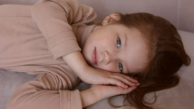 Portrait of 6-year-old little girl laying on her back in casual outfit, on sofa at home. Female child pretty face with beautiful deep eyes. Cute baby girl smiling. Relax and peace. Turtleneck clothes