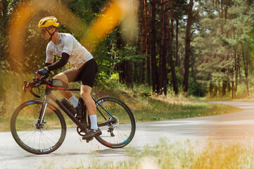 Young male cyclist trains outside the city in the woods on the road. Riding a bike.