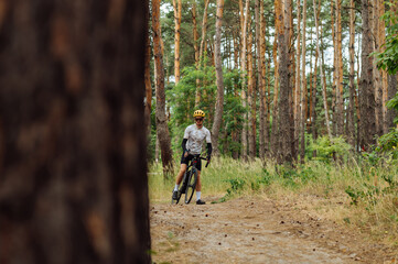 Male cyclist athlete standing in the woods on the road among the trees. Cyclist training in the woods.
