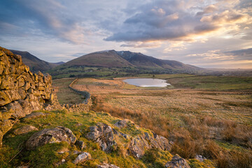 Beautiful morning looking toward Blencathra in the English Lake District as the sun rises, with warm light on the stone wall and a tarn in the distance