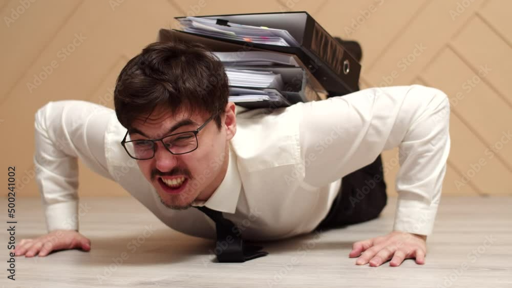 Poster male office worker is pinned down by stack folders of working documents and tries to get up from flo