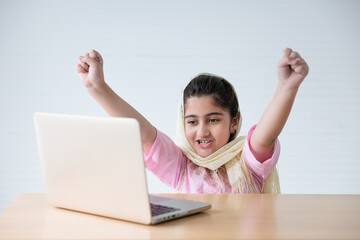 muslim girl using a laptop computer and raised hand for celebrating good news on the table