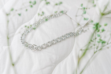Silver bijouterie chain on white textile background.