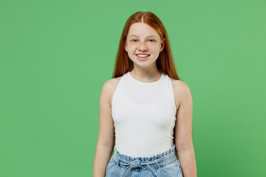 Little redhead kid smiling happy fun cool cheerful girl 12-13 years old wearing white tank shirt looking camera isolated on plain green color background studio portrait. Childhood lifestyle concept.