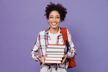 Fototapeta Young smiling fun girl woman of African American ethnicity teen student in shirt backpack hold pile of books isolated on plain purple background. Education in high school university college concept. obraz