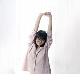 Fototapeta premium Standed Little Asian young Glasses Girl stretches oneself in front of light white curtain background.