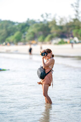 Smart Asian Woman takes a photo with her Digital Camera on the beach in afternoon Sunlight.