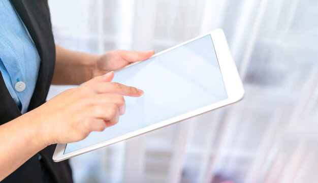 Close up to the White empty screen tablet which hold by Asina women in black suit in front of transparent curtain