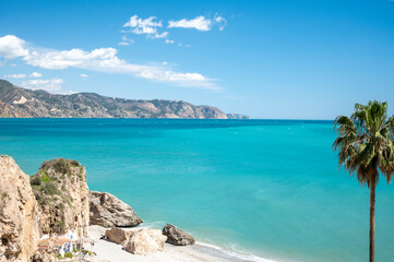 Travel destination, view on sandy beach, blue sea and mountains from Balcon de Europa in small Andalusian town Nerja with white houses and narrow streets on Costa del Sol, Spain