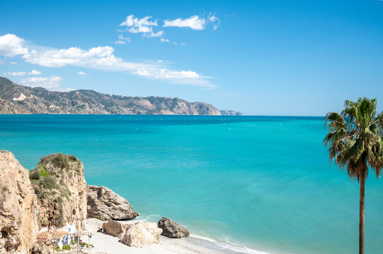 Travel destination, view on sandy beach, blue sea and mountains from Balcon de Europa in small Andalusian town Nerja with white houses and narrow streets on Costa del Sol, Spain