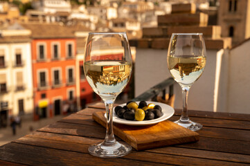 Two glasses of Spanish dry rueda white wine served with olives on roof terrace with view on old part of Andalusian town Granada, Spain