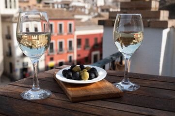 Two glasses of Spanish dry rueda white wine served with olives on roof terrace with view on old part of Andalusian town Granada, Spain