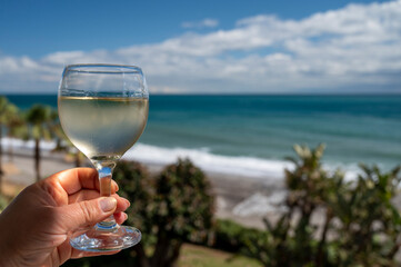 Hand with glass of Spanish dry white wine on beach terrace with view on Mediterranean sea