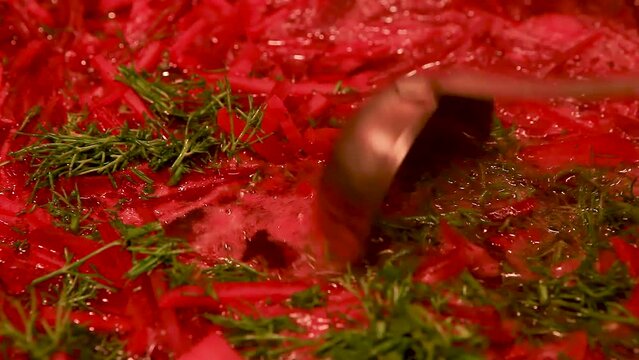 Cooking at home. Macro shot of the surface of borscht in a saucepan, sprinkled with fresh dill. Hot red beetroot soup is stirred with a ladle, the pan is covered with a lid.