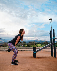 Young blonde woman performing calisthenics exercises in an urban park. She is doing kettlebell...