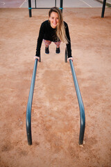 Young blonde woman performing calisthenics exercises in an urban park. She is exercising on the...