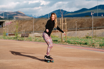 Young blonde woman practicing skateboarding in public park.