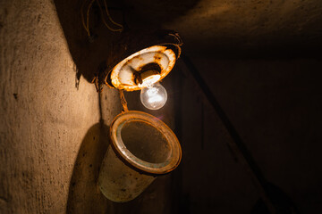An old incandescent light bulb in an old rusty ceiling lamp in a dark basement close-up