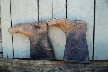 Dirty rubber boots standing against a wooden plank wall after work is done. The boots were turned...