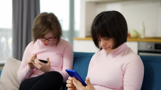 Two girls with down syndrome are holding smartphones -looking at photos, use a social media app