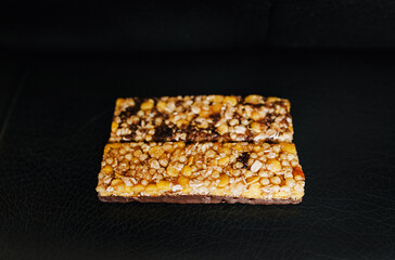 Two small sweet bars of muesli, dried apricots, grapes, nuts, cereal lie on a black sofa. Close-up photo of the dessert. Healthy food.