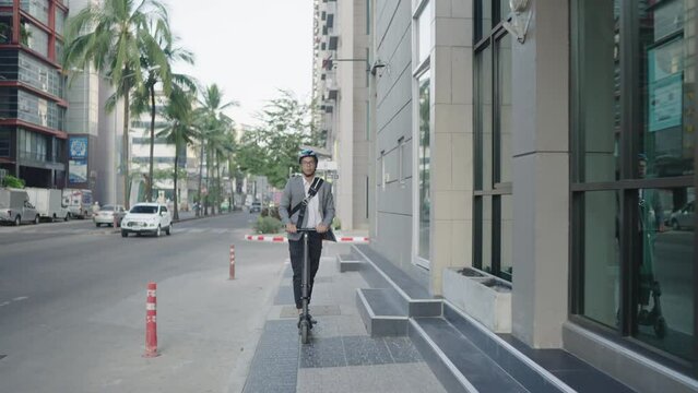 A businessman in a suit, wearing a helmet, wearing glasses, riding a scooter out to work on the streets of urban lifestyle. In the morning time.Concept Business lifestlye eco.
