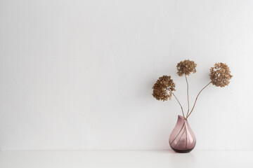White desk with minimal vase with a decorative dried branches, flower against white wall.
