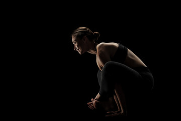 Fototapeta na wymiar cute caucasian girl exercising yoga poses against dark backgroung. side lit silhouette.