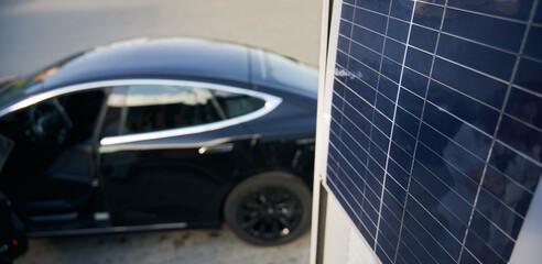 On the blurred backdrop of black elite car close up view of one solar panel. Concept ecological...