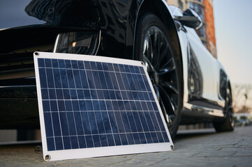 Black electric vehicle and photovoltaic solar panel on city street. Concept environmental...