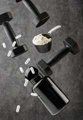 Capsules of sports supplements, a scoop with protein and dumbbells levitate on a dark background. The concept of sports nutrition and supplements.
