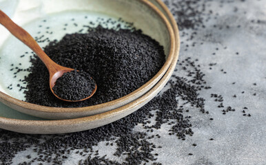 Plate of Indian spice Black cumin (nigella sativa or kalonji) seeds close up with a wooden spoon