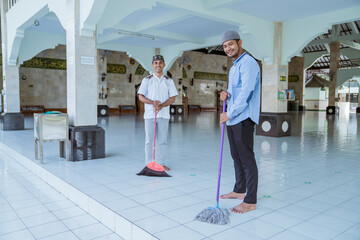 two asian muslim male cleaning the mosque using broom and sweeping the floor