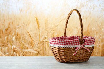 Empty picnic basket on wooden white table over wheat field blurred background. Shavuot holiday mock...