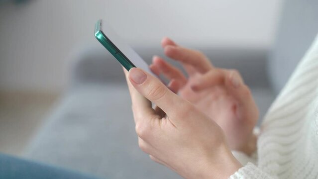 Close-up of beautiful female hands with a modern smartphone. The girl is viewing the content of the online store. Side view.