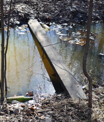 An improvised makeshift bridge made of a single wooden plank across a ditch with water